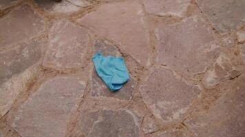 Discarded blue surgical mask lying on a textured stone pavement. video