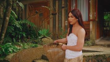 Serene woman holding a basket near a rustic cabin surrounded by lush greenery. video