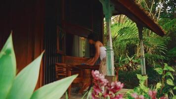 person arbetssätt på en bärbar dator på en trä- veranda omgiven förbi frodig tropisk lövverk. video