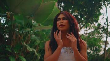 Portrait of a thoughtful woman with long hair standing amidst lush greenery, looking away with a contemplative expression video