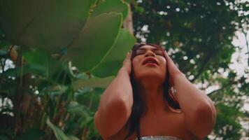 Serene woman with closed eyes enjoying nature, surrounded by lush green foliage. video