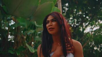 portrait de une réfléchi femme avec rouge cheveux permanent dans une tropical jardin, grand vert feuilles dans le Contexte video