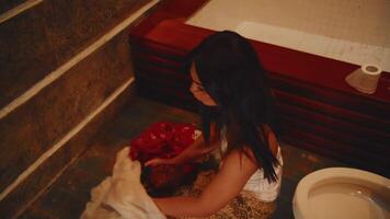 Emotional woman holding a white cloth with red embroidery, sitting on stairs in a dimly lit environment. video