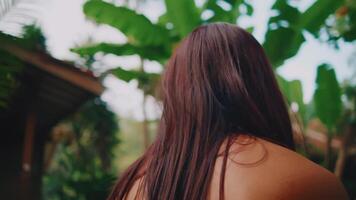 Over-the-shoulder view of a woman gazing at a tropical garden with lush greenery and a wooden gazebo video