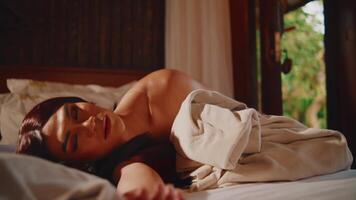 un' donna nel un' bianca vestito è addormentato pacificamente su un' confortevole letto nel sua camera video