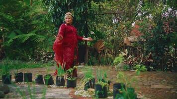 elegant vrouw in rood jurk wandelen door een weelderig tuin na regenen, met levendig groen video