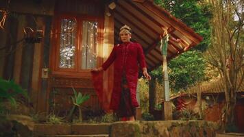 Woman in traditional red attire posing on steps of a rustic cabin surrounded by lush greenery. video