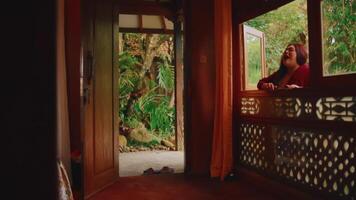 persoon staren uit van een traditioneel houten deuropening op een sereen tuin met weelderig groen. video