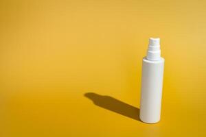 Blank white spray bottle on yellow background in direct sunlight photo