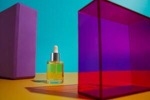 Face oil in glass bottle on yellow and blue background with pink and purple geometric elements photo