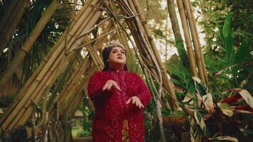 Elegant woman in a red dress and golden crown posing in a bamboo forest. video
