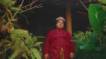 Woman in traditional attire performing a dance outside a rustic building, with greenery video