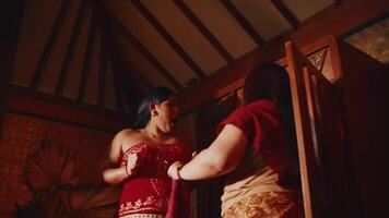 twee Dames in traditioneel kleding hebben een gesprek in een vaag verlicht, rustiek interieur met houten balken. video