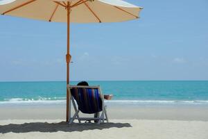 People sitting on lounge chairs on tropical beach under umbrellas, white sand, sea, chill, relax, vacation photo