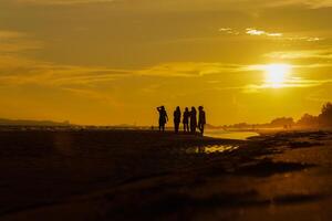 Silhouette of a group of friends enjoying the sunset on the beach at golden sunset time, relaxing on a relaxing vacation, sea in the evening. photo