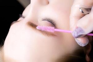 close-up of the model's dyed and laminated hairs, the master holds a brush in front of the eyebrows photo