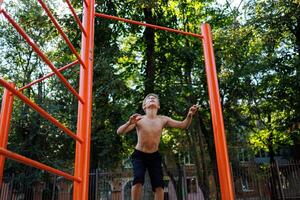 An athletically built child in the park tries to jump up and grab the crossbar. Street workout on a horizontal bar in the school park. photo