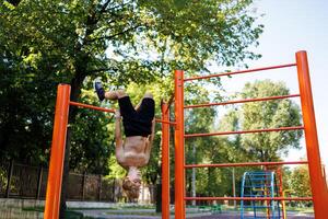 yendo en para Deportes chico colgando al revés abajo. calle rutina de ejercicio en un horizontal bar en el colegio parque. foto