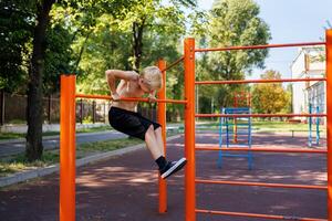 The boy is trying to climb the sports bar. Street workout on a horizontal bar in the school park. photo