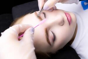 the master combs the eyebrows with a brush after the procedure of lamination and eyebrow coloring photo