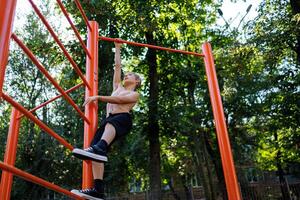 An athletic teenager tries to climb the crossbar. Street workout on a horizontal bar in the school park. photo