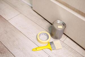 A can of paint and a paintbrush are on the floor. Repair staining the doors with paint. photo