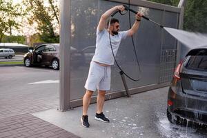 At a car wash, a man washes off the foam by lifting it over his head with a water cannon. A car at a self service car wash. photo