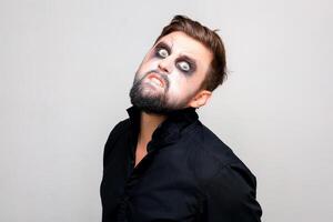 a bearded man with undead-style makeup on Halloween looks with big eyes at the camera photo