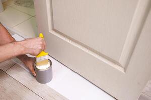 The hand that holds the brush dips it in the paint. Repair staining the doors with paint. photo