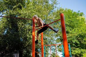 A boy athlete climbs a horizontal bar to perform a formal element. Street workout on a horizontal bar in the school park. photo