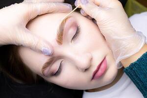 close-up alignment of the contour of the eyebrows with a cotton swab after the procedure lamination and coloring of the eyebrows photo