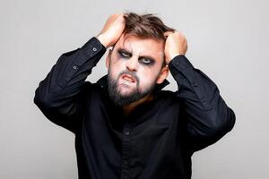 un hombre con un barba y maquillaje para Víspera de Todos los Santos agarrado su pelo con su manos foto