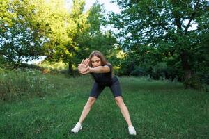 A young girl doing exercises in the park. Athletic girl in a tight uniform working outdoors in the park. photo