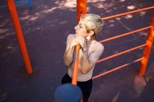 deportivo niño realiza lado levantar en el encimera. calle rutina de ejercicio en un horizontal bar en el colegio parque. foto