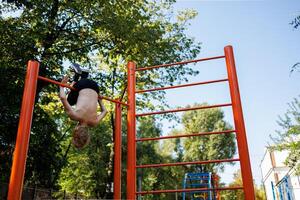 A teenager on a tourniquet performs acrobatic elements. Street workout on a horizontal bar in the school park. photo