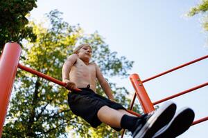 Bottom view of a teenage gymnast who performs the elements. Street workout on a horizontal bar in the school park. photo