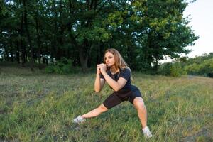 A girl in nature performs stretching of leg muscles. Athletic girl in a tight uniform working outdoors in the park. photo