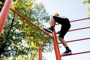 Bottom view of a teenager boy who climbs on a sports horizontal bar. Street workout on a horizontal bar in the school park. photo