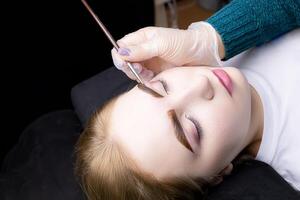 in the hands of the master, a thin brown brush with which he applies eyebrow paint to the hairs after the lamination procedure photo