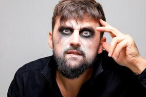 portrait of a bearded man with undead-style makeup who holds his hand near his head photo