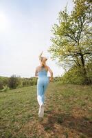 A view of a girl of athletic build running through the park. Beautiful blonde Caucasian woman in blue tight tracksuit. Blonde girl at an outdoor training session photo