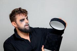 a bearded man with makeup for Halloween opens a black gift box photo