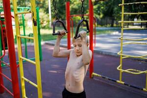 un atlético adolescente sostiene sobre el pasamanos de un Deportes simulador. calle rutina de ejercicio en un horizontal bar en el colegio parque. foto