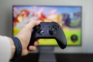 A hand holds a game controller in front of the monitor, game gamepad in hand photo