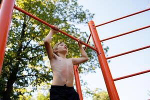 Bottom view of a boy gymnast holding onto a gymnastics bar. Street workout on a horizontal bar in the school park. photo