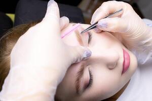 the master's hands in white gloves stretch the eyebrow and pluck out excess eyebrow hairs with tweezers photo