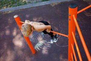 A teenager stretched out holding onto his arms and performing acrobatic exercises on a horizontal bar. Street workout on a horizontal bar in the school park. photo