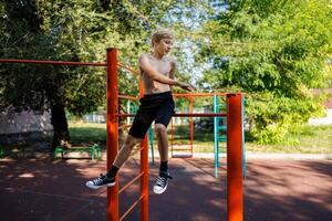 The teenager plays sports. Street workout on a horizontal bar in the school park. photo