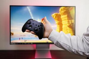 In the background of a game monitor, a man's hand holds a controller in the palm of his hand. game gamepad in hand photo