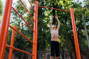 An athletic child in the park tries to jump up and grab the bar. Street workout on a horizontal bar in the school park. photo